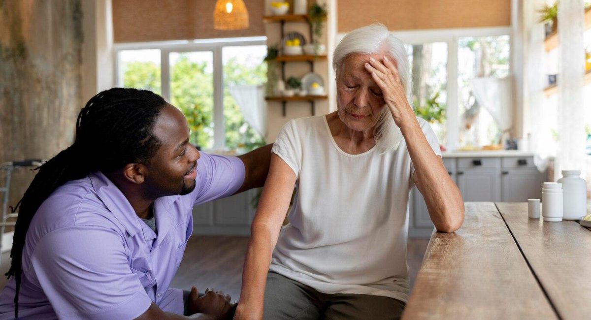 A tired family caregiver rests at a kitchen table after caring for her elderly mother, highlighting the often unseen sacrifices of caregivers.