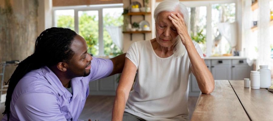 A tired family caregiver rests at a kitchen table after caring for her elderly mother, highlighting the often unseen sacrifices of caregivers.